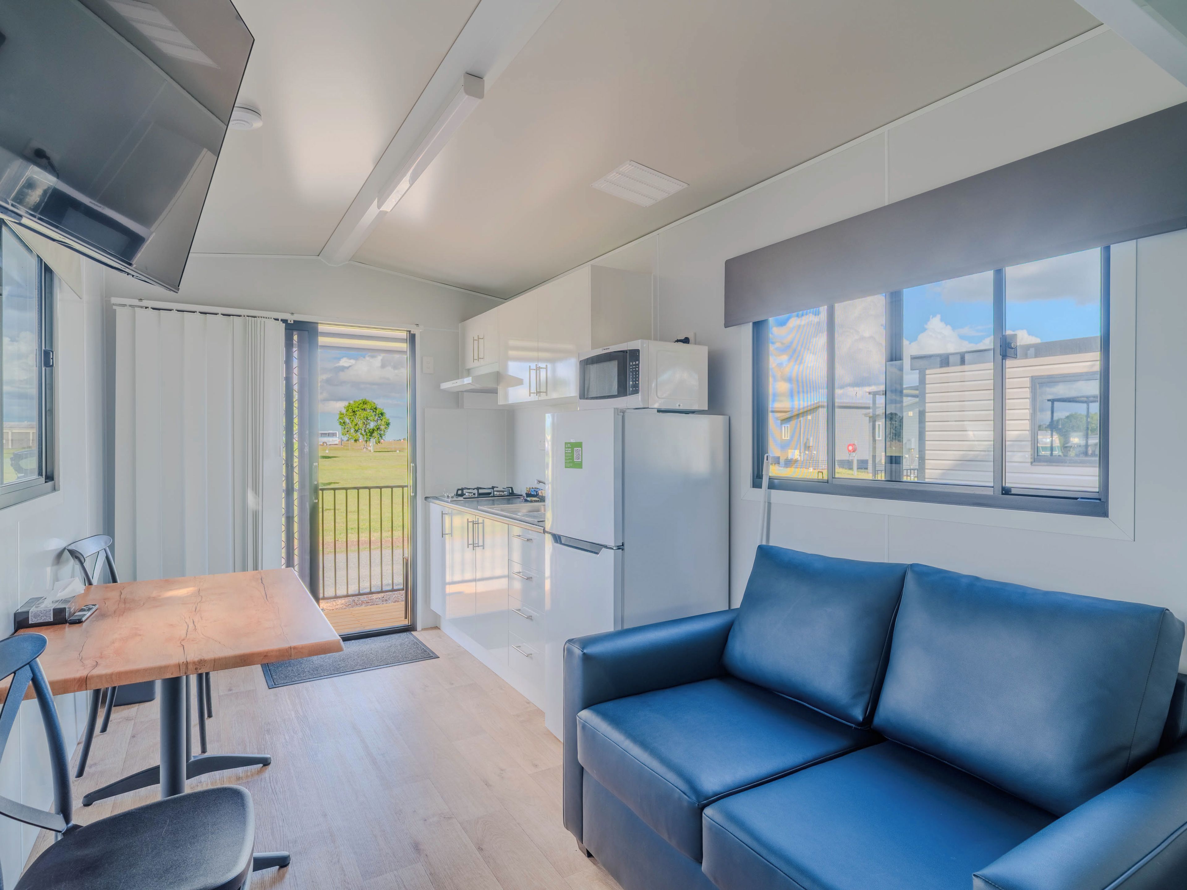 A modern kitchen with white cabinets, a microwave, and a refrigerator. There is a dining table with chairs and a blue sofa.