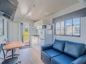 A modern kitchen with white cabinets, a microwave, and a refrigerator. There is a dining table with chairs and a blue sofa.