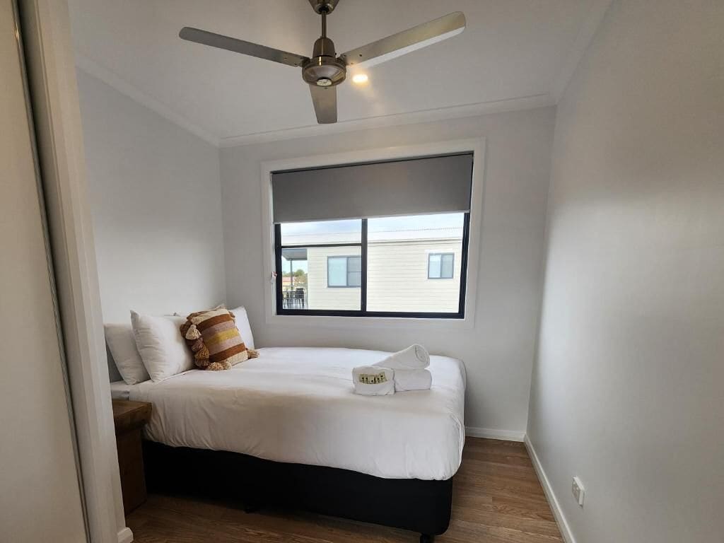 Een slaapkamer met een bed, een plafondventilator, een raam en uitzicht op een gebouw.