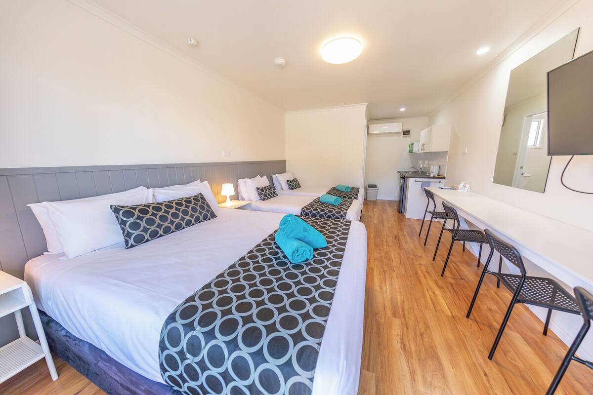A hotel room with two beds, a desk, and a kitchenette.