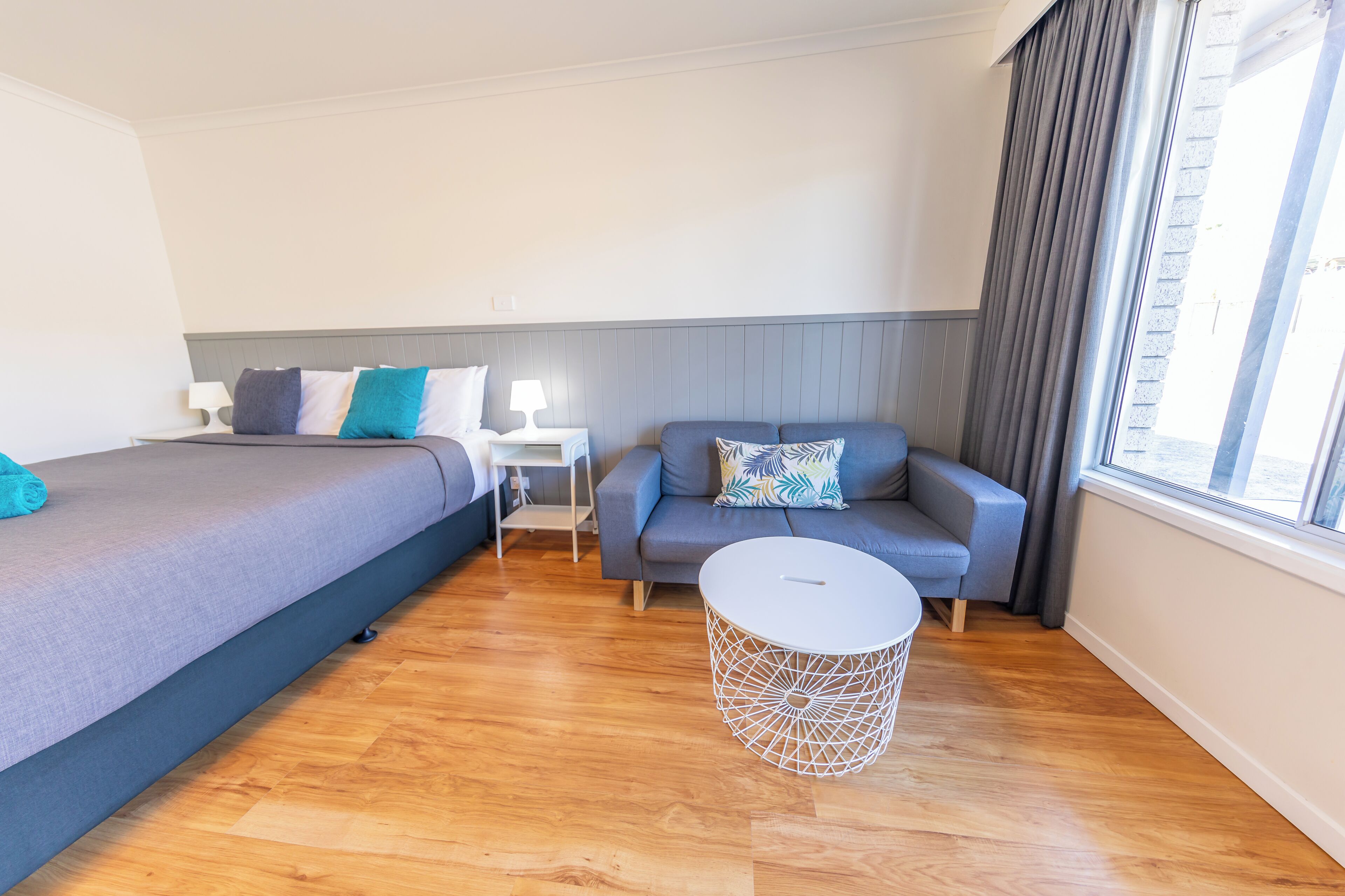 Ein modernes Hotelzimmer mit Bett, einer Couch, einem kleinen Tisch und einem Fenster mit Vorhängen.
