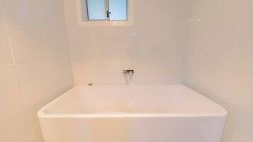 A bathroom with a white bathtub, a window above it, and white tiled walls.