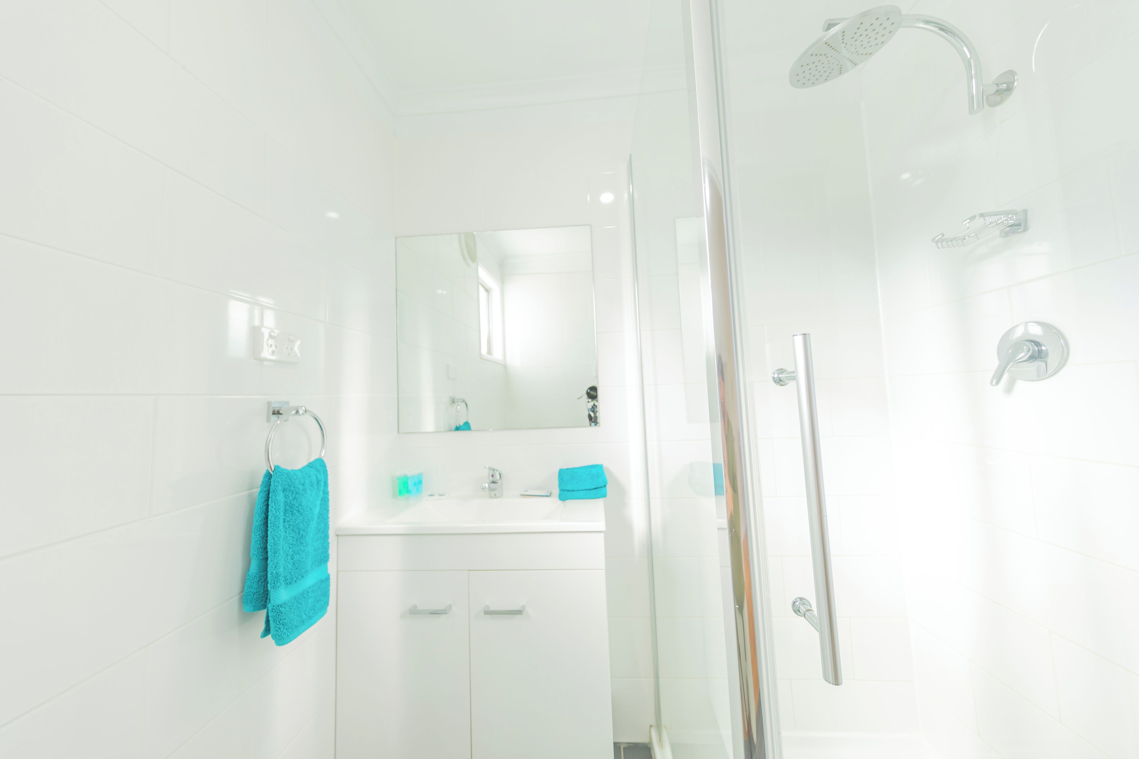 Une salle de bain moderne avec une douche à parois de verre, un meuble-lavabo blanc avec un miroir et un porte-serviettes.