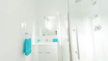 Une salle de bain moderne avec une douche à parois de verre, un meuble-lavabo blanc avec un miroir et un porte-serviettes.