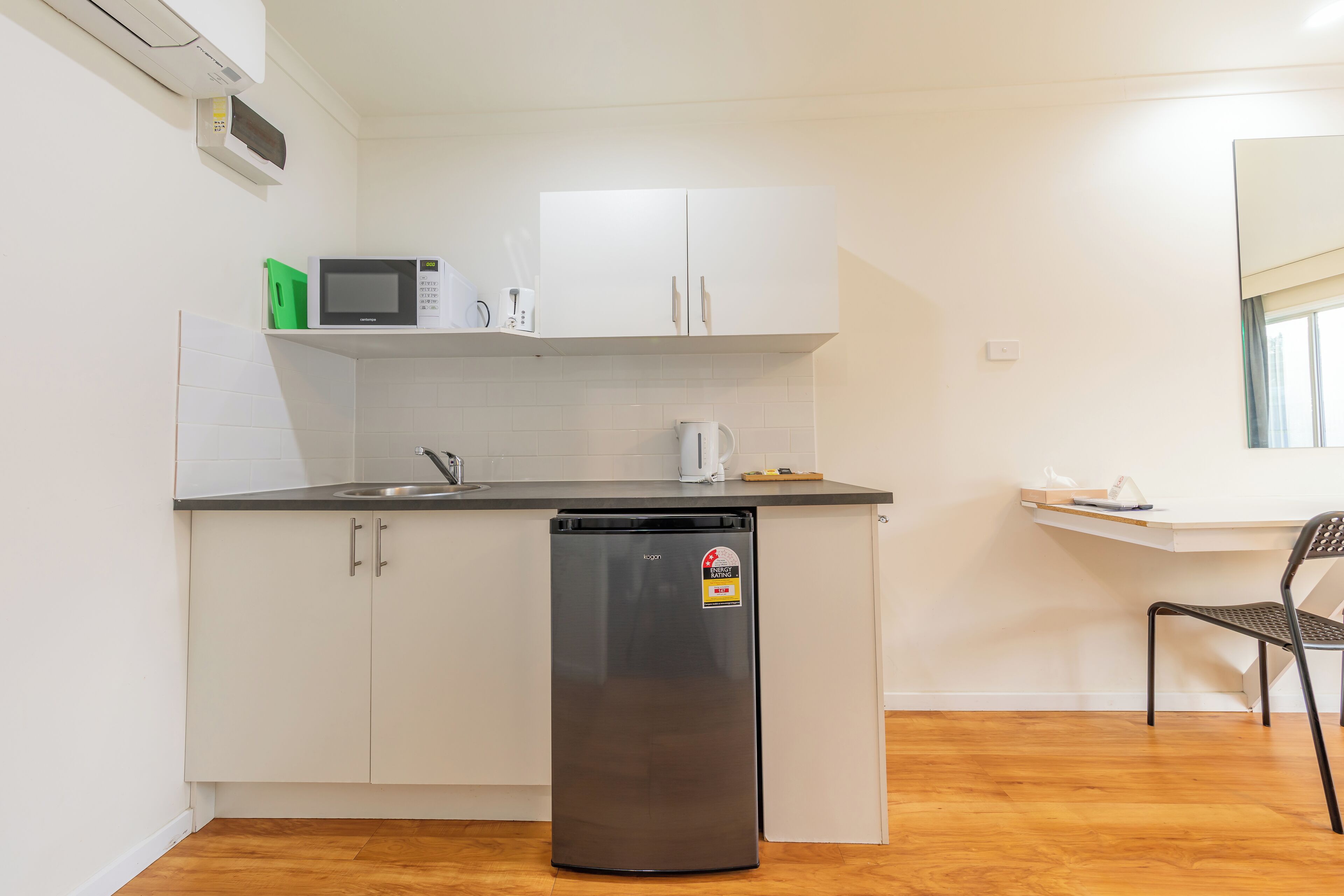A compact kitchen with white cabinets, a black refrigerator, a microwave, and a coffee maker.