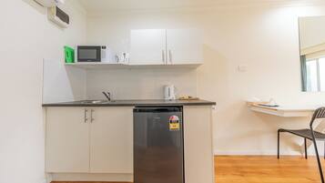 A compact kitchen with white cabinets, a black refrigerator, a microwave, and a coffee maker.