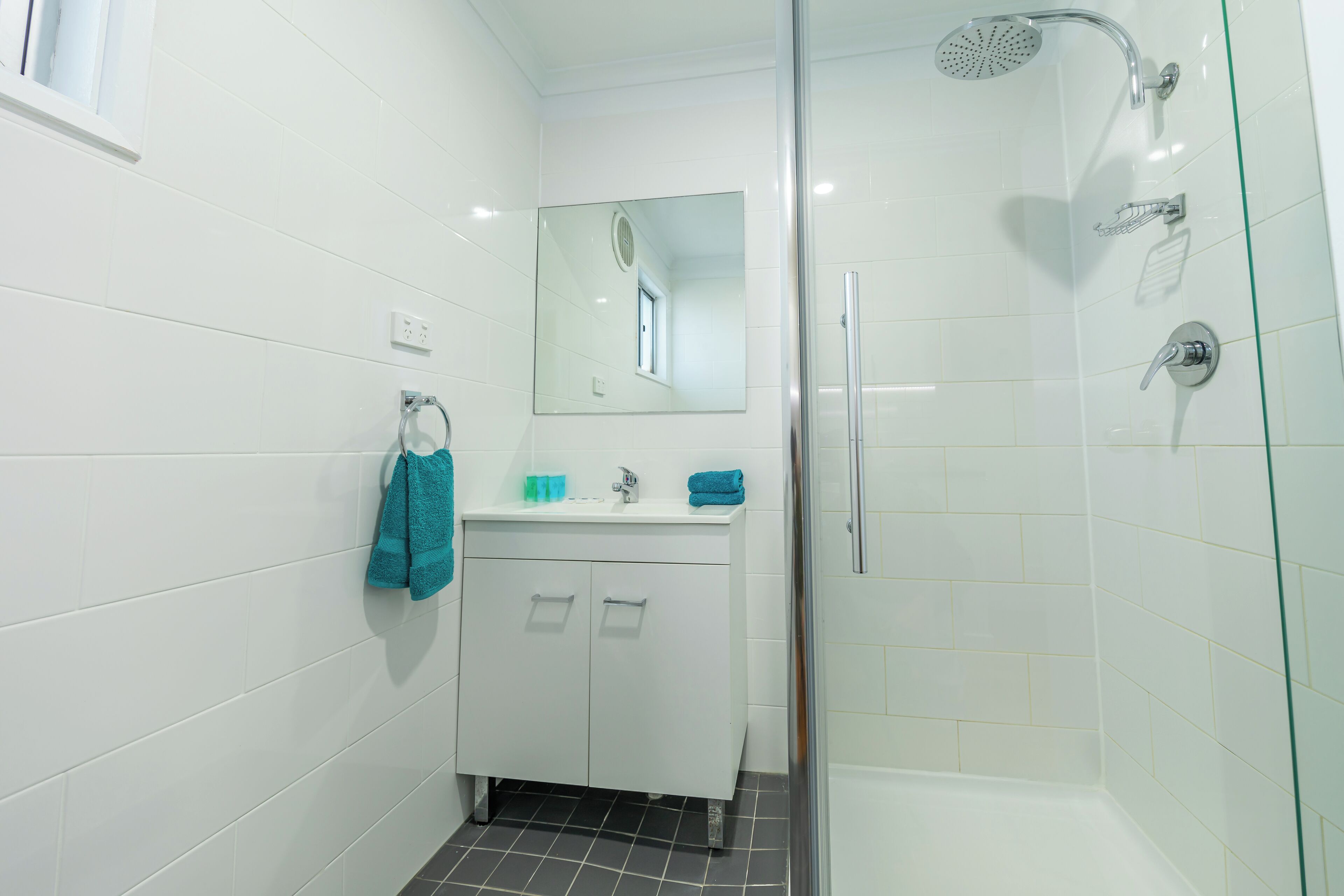 Un baño moderno con azulejos blancos, mampara de ducha de vidrio, lavamanos con espejo y toallero.