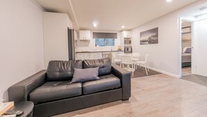 Una sala de estar moderna con un sofá de cuero negro, una mesita con un control remoto, y vistas a una cocina y comedor al fondo.