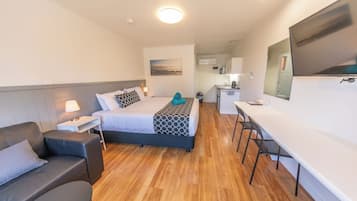 A modern hotel room with a bed, a desk, a chair, and a small kitchenette.