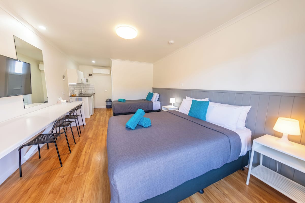 A hotel room with a large bed, a desk with chairs, a kitchenette, and a bathroom.