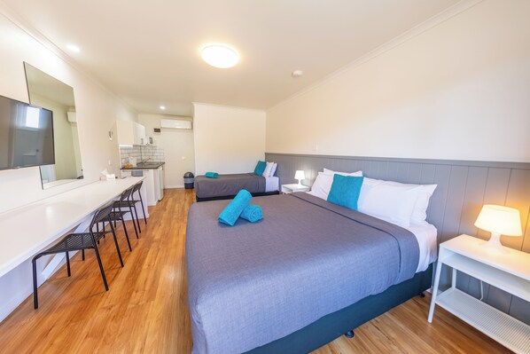 Une chambre d’hôtel avec un grand lit, un bureau avec des chaises, une kitchenette et une salle de bain.