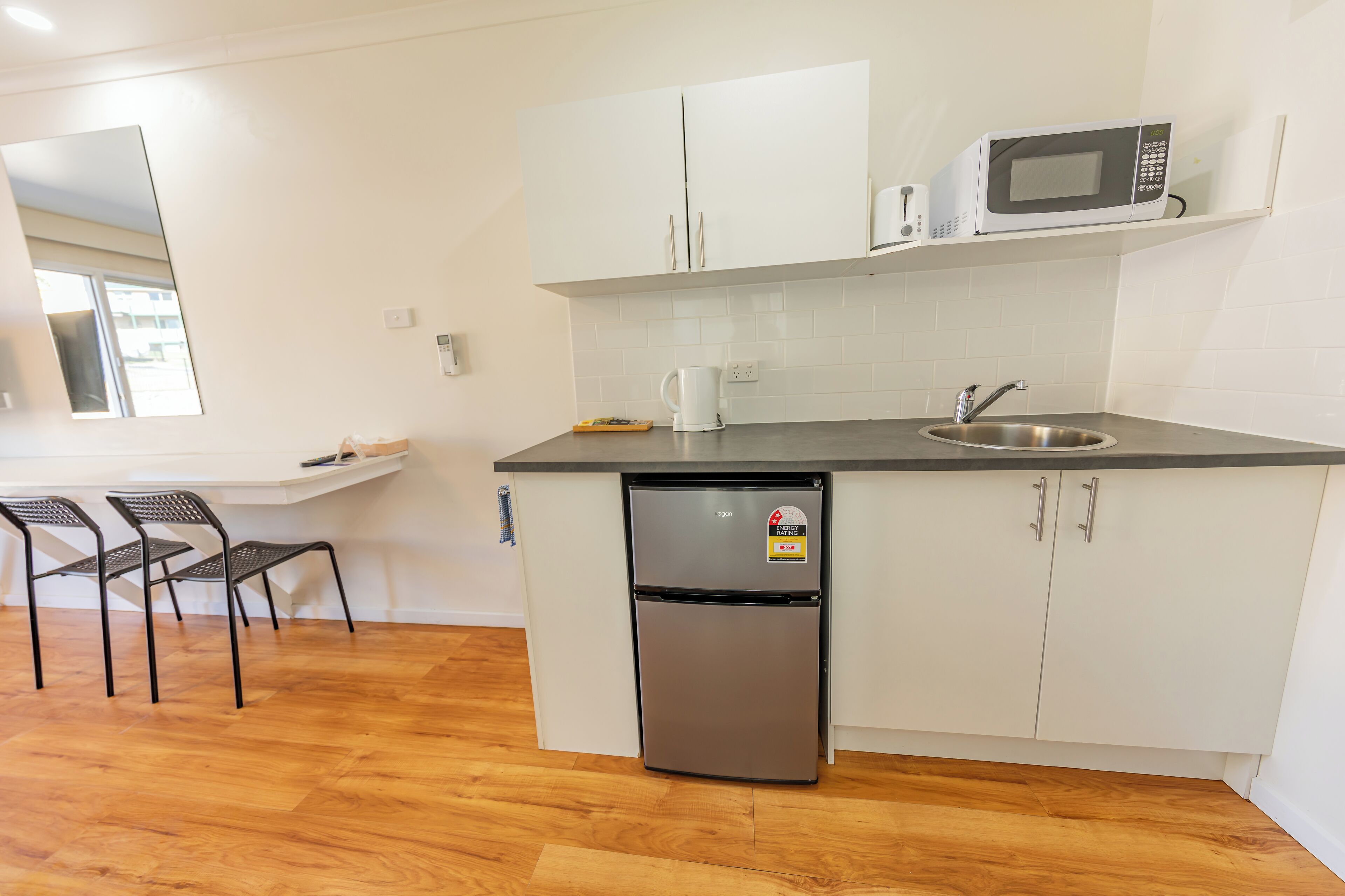 A compact kitchen with a refrigerator, microwave, and sink. There are two chairs and a small table.