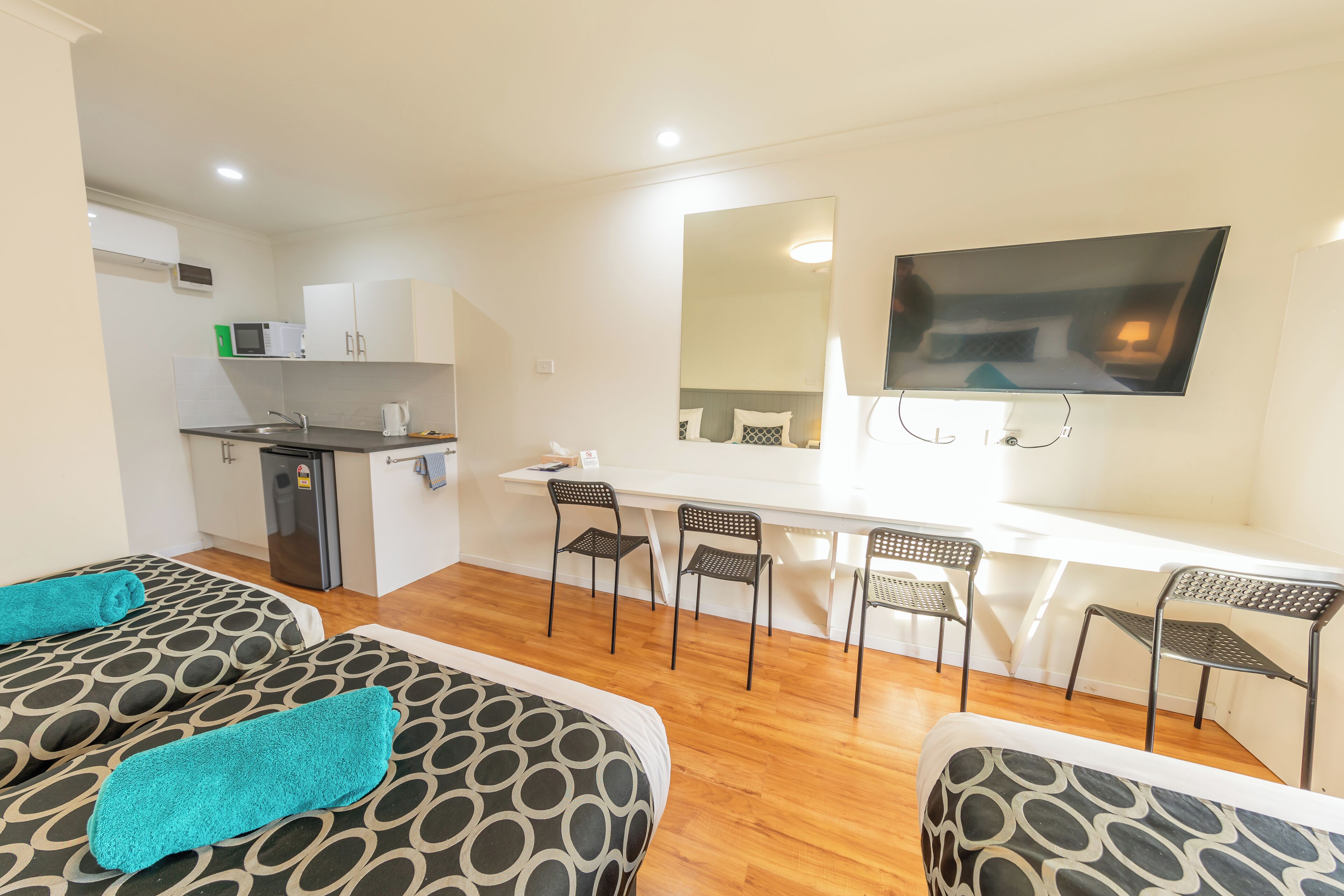 Una habitación de hotel moderna con kitchenette, un televisor de pantalla plana en la pared y dos camas con ropa de cama estampada.