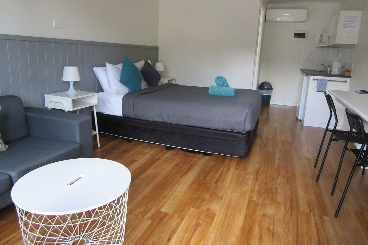 A compact hotel room with a bed, a small desk, a chair, a sofa, and a round table.