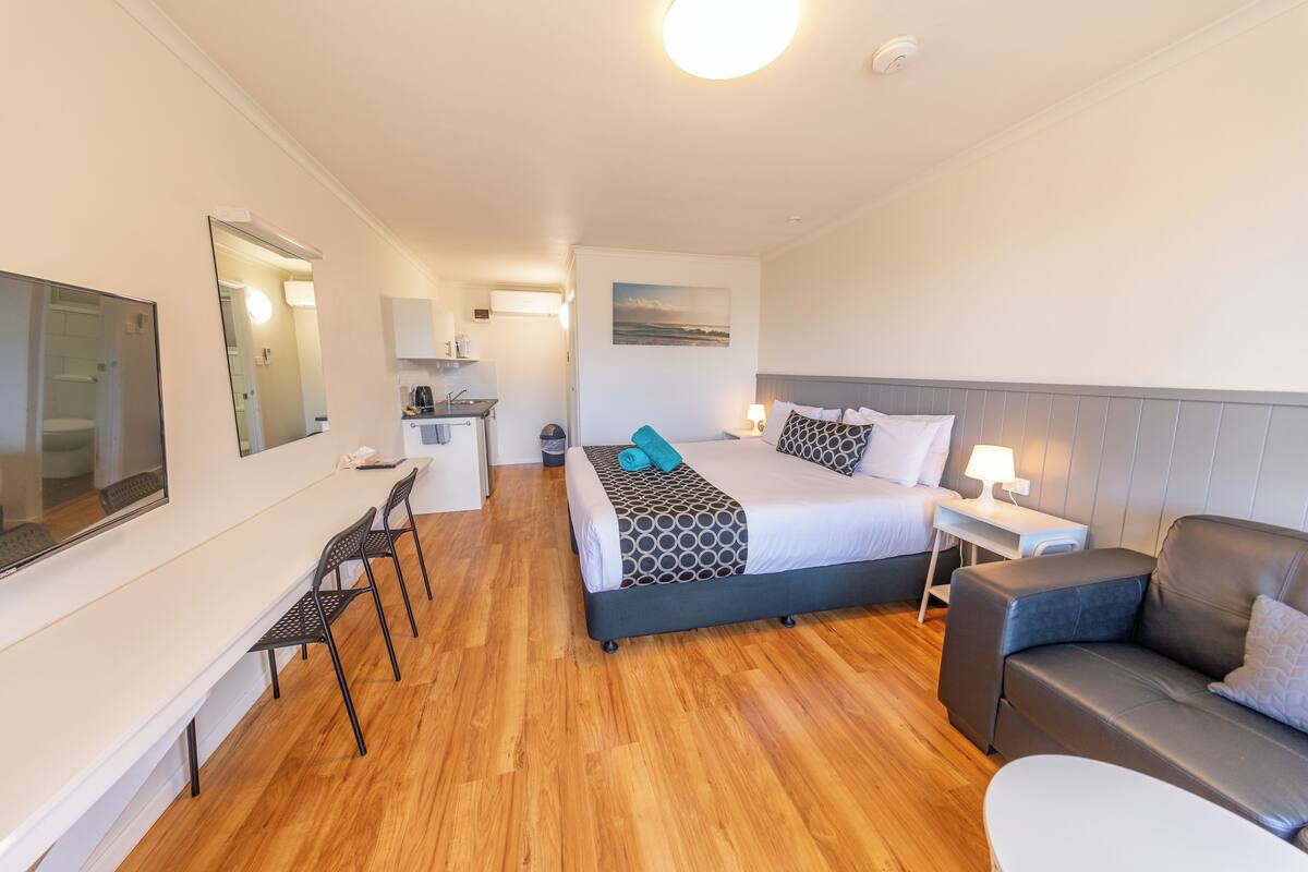A hotel room with a bed, a desk, a chair, a sofa, and a TV.