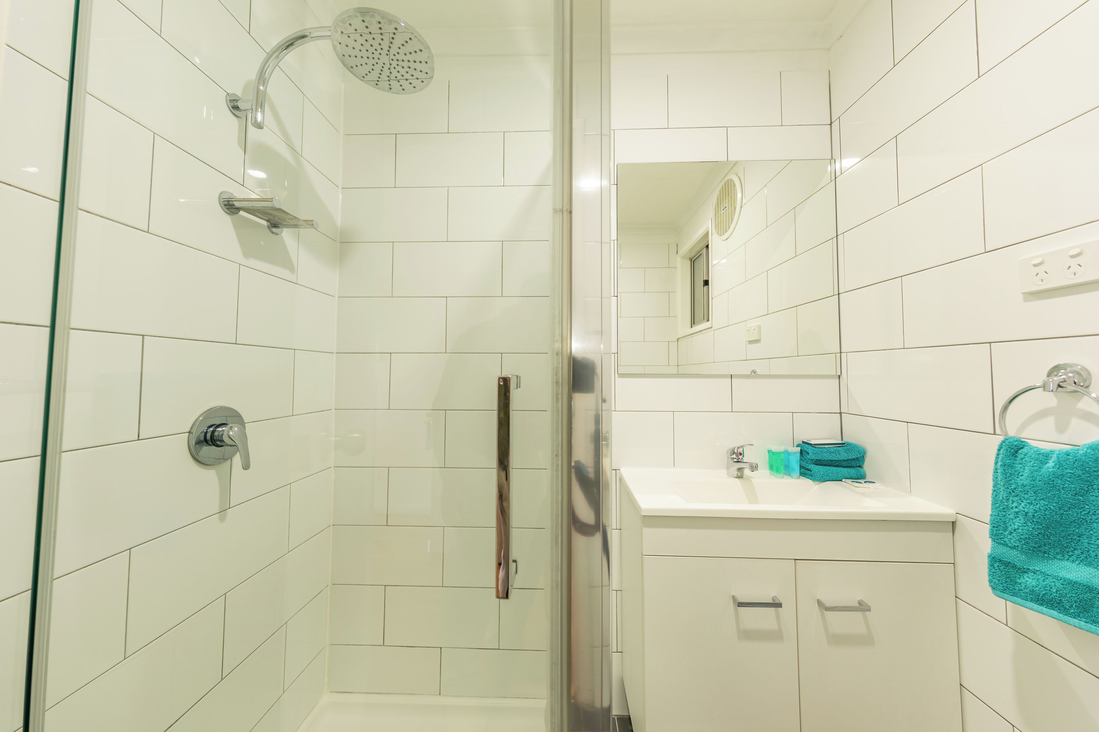 A modern bathroom with white tiles, a glass shower enclosure, a sink with a mirror, and a towel rack.