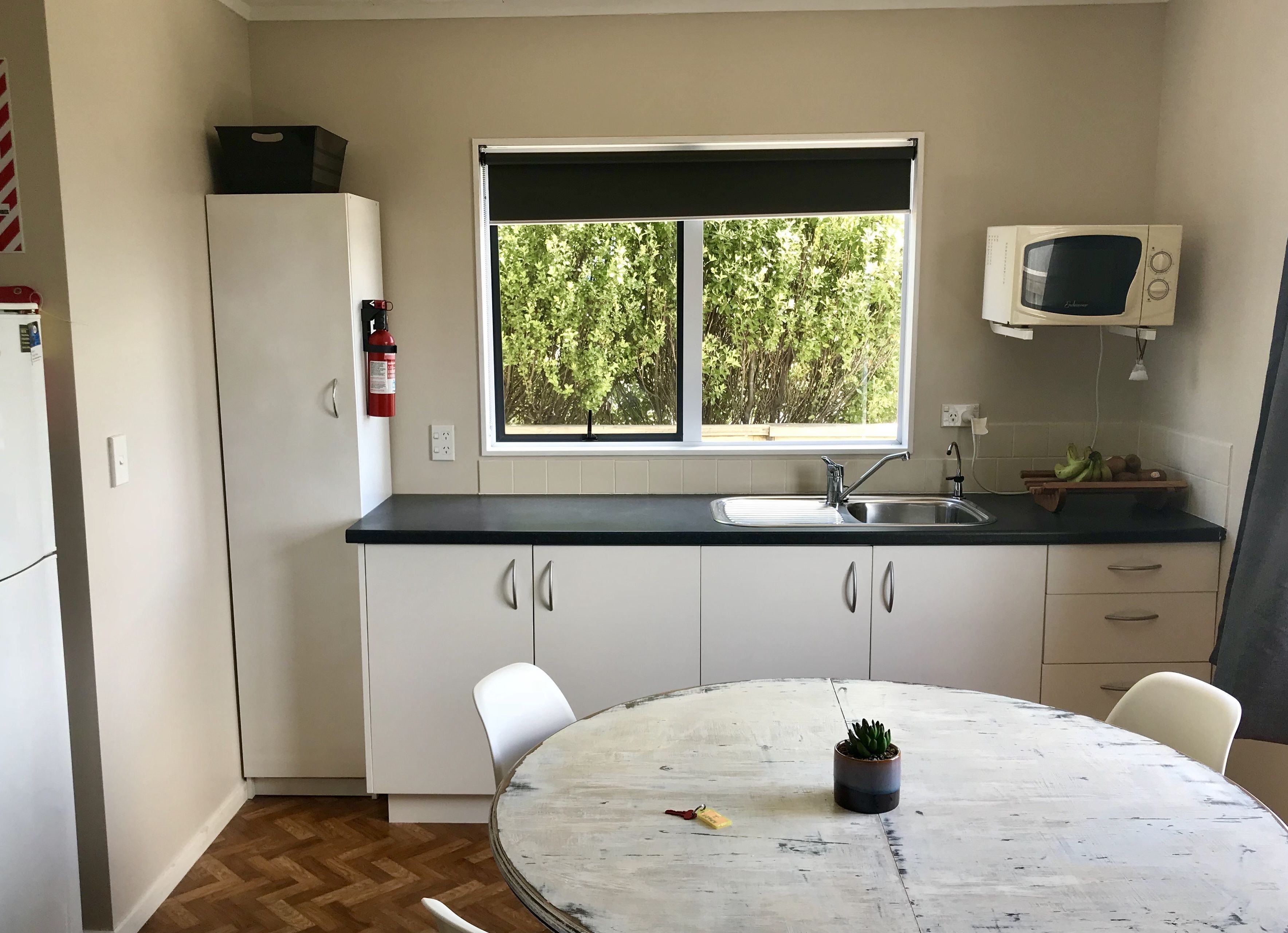 Een kleine keuken met een raam, een magnetron en een spoelbak.