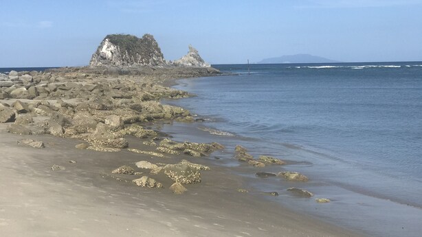 Ein felsiger Strand mit großen Steinen und freiem Blick auf den Ozean.