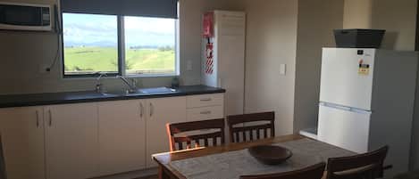 A compact kitchen with a window, a microwave, a refrigerator, and a dining area with chairs and a table.