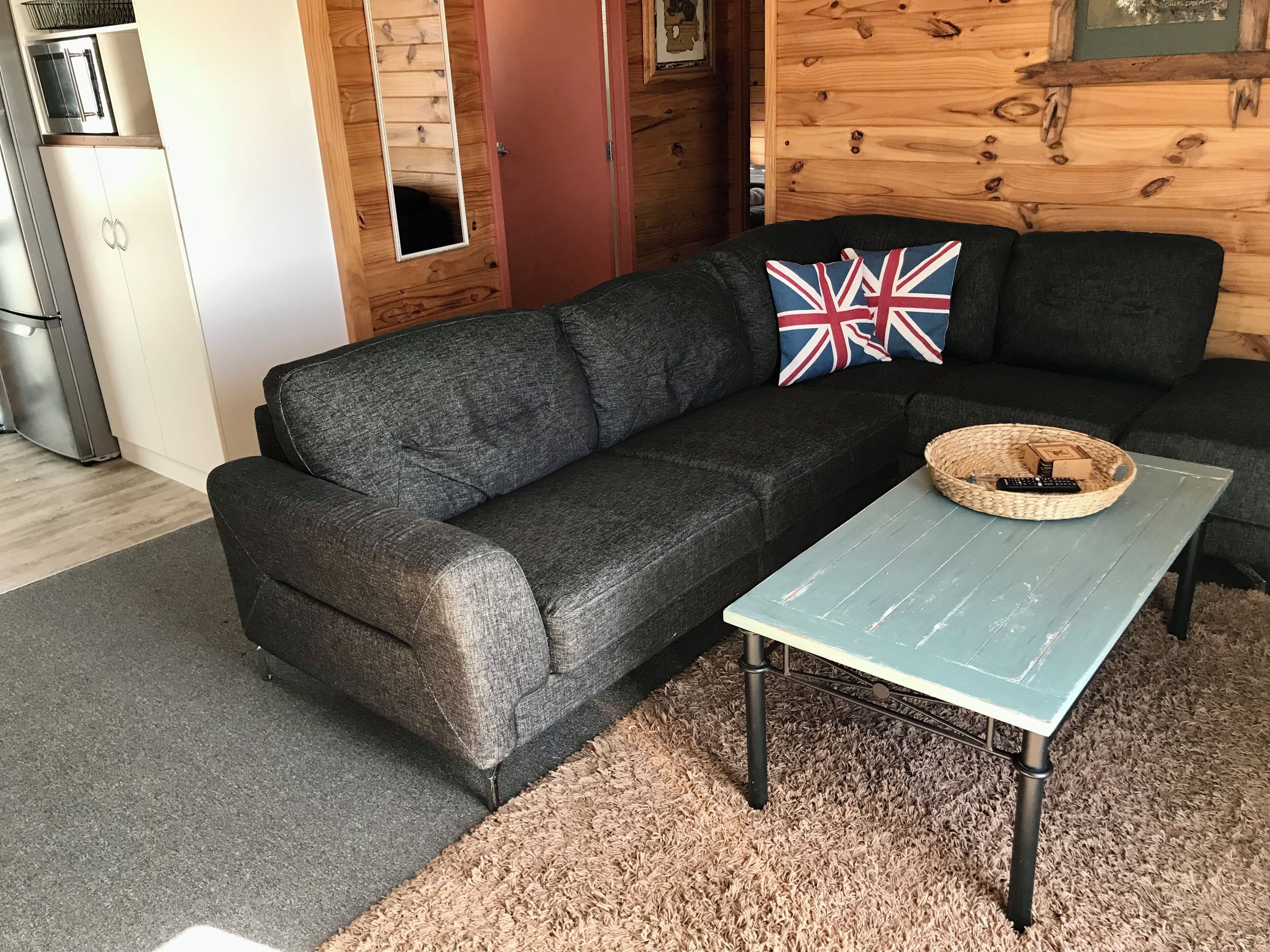 A cozy living room with a dark grey sofa, a woven coffee table, and a small rug.