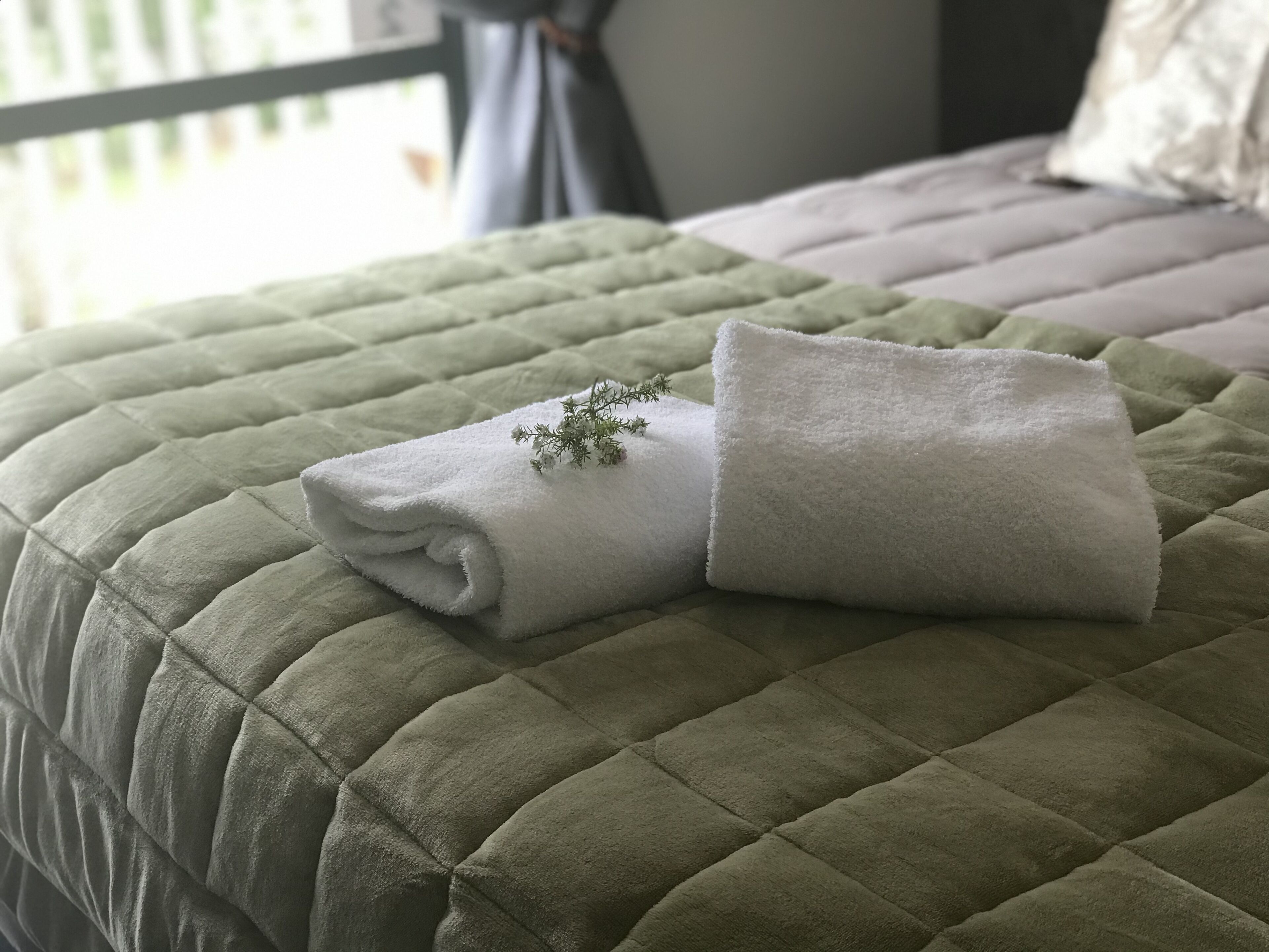 Un lit bien fait, recouvert d’une courtepointe matelassée verte, avec deux serviettes blanches pliées posées sur le dessus.
