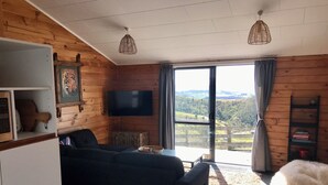 Ein gemütliches Wohnzimmer mit großem Fenster, Holzwänden, einem Flachbildfernseher und einer bequemen Sitzecke.