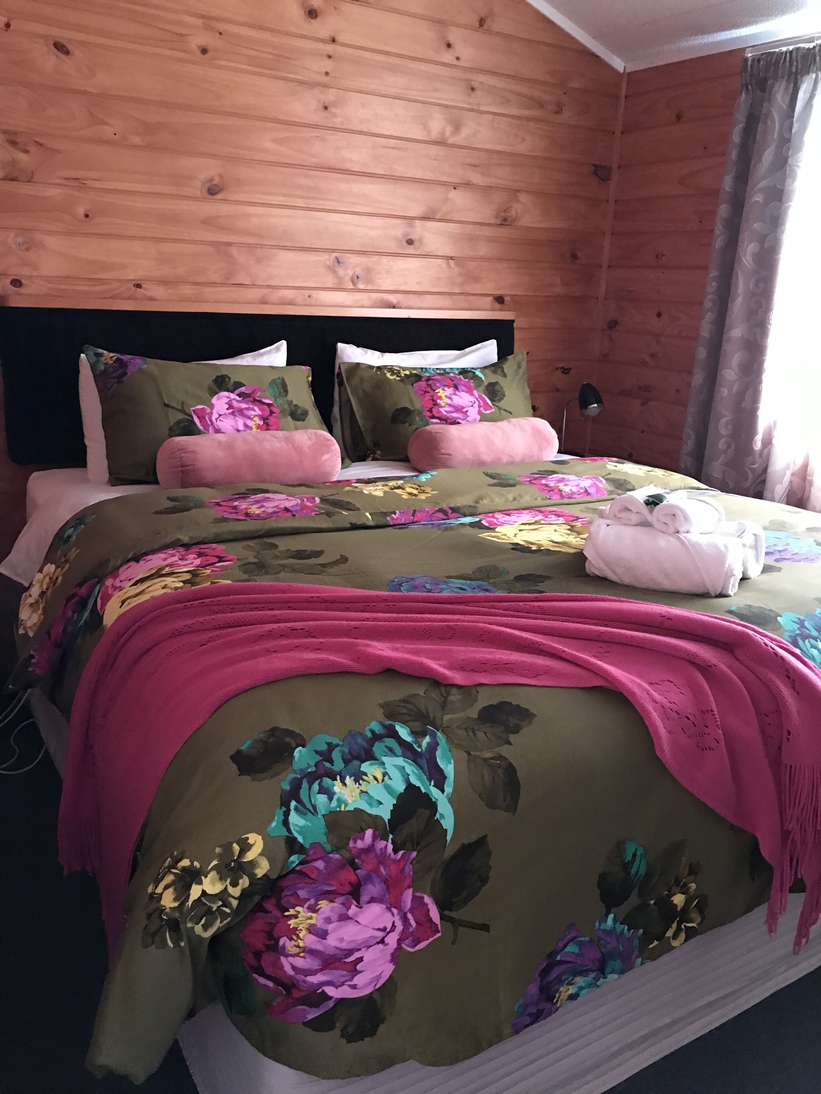 A wooden-paneled room with a bed featuring floral bedding and pink accents.