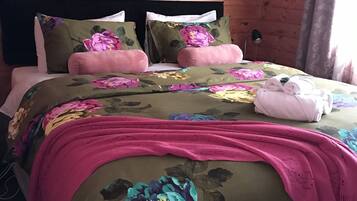 A wooden-paneled room with a bed featuring floral bedding and pink accents.