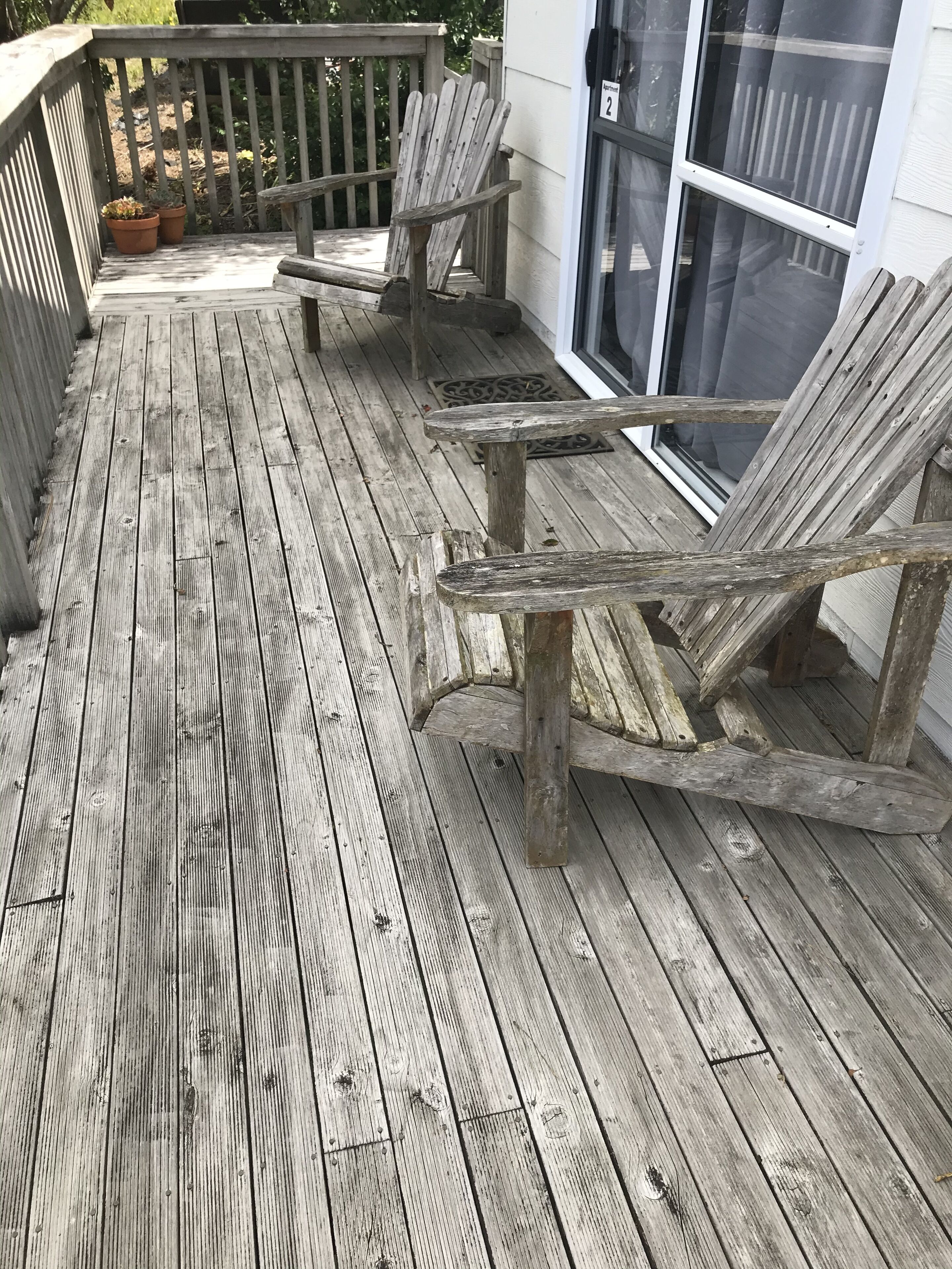 A wooden deck with two Adirondack chairs and a potted plant.