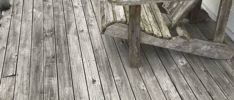 A wooden deck with two Adirondack chairs and a potted plant.