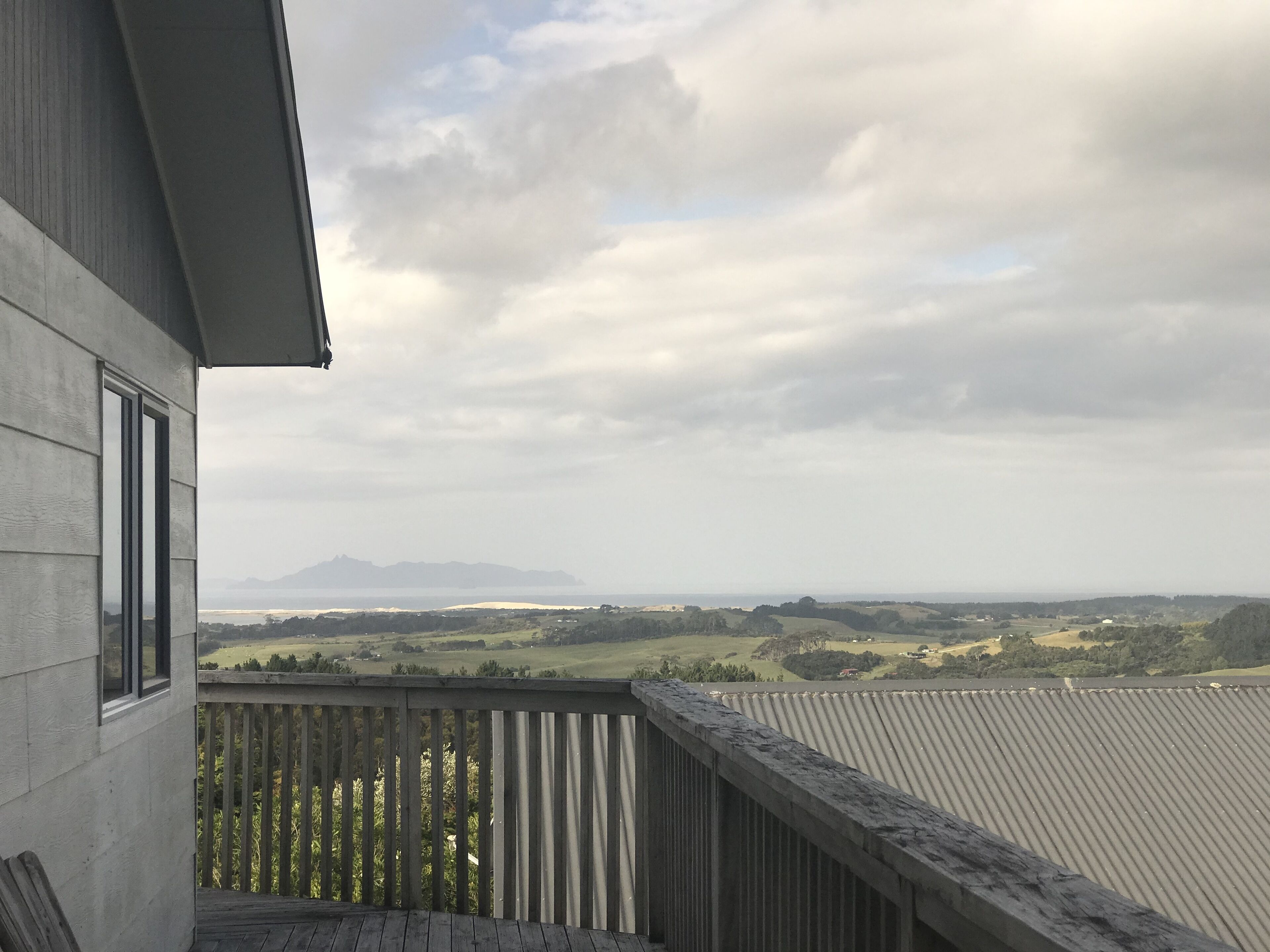 A balcony with a view of a hilly landscape and distant mountains.