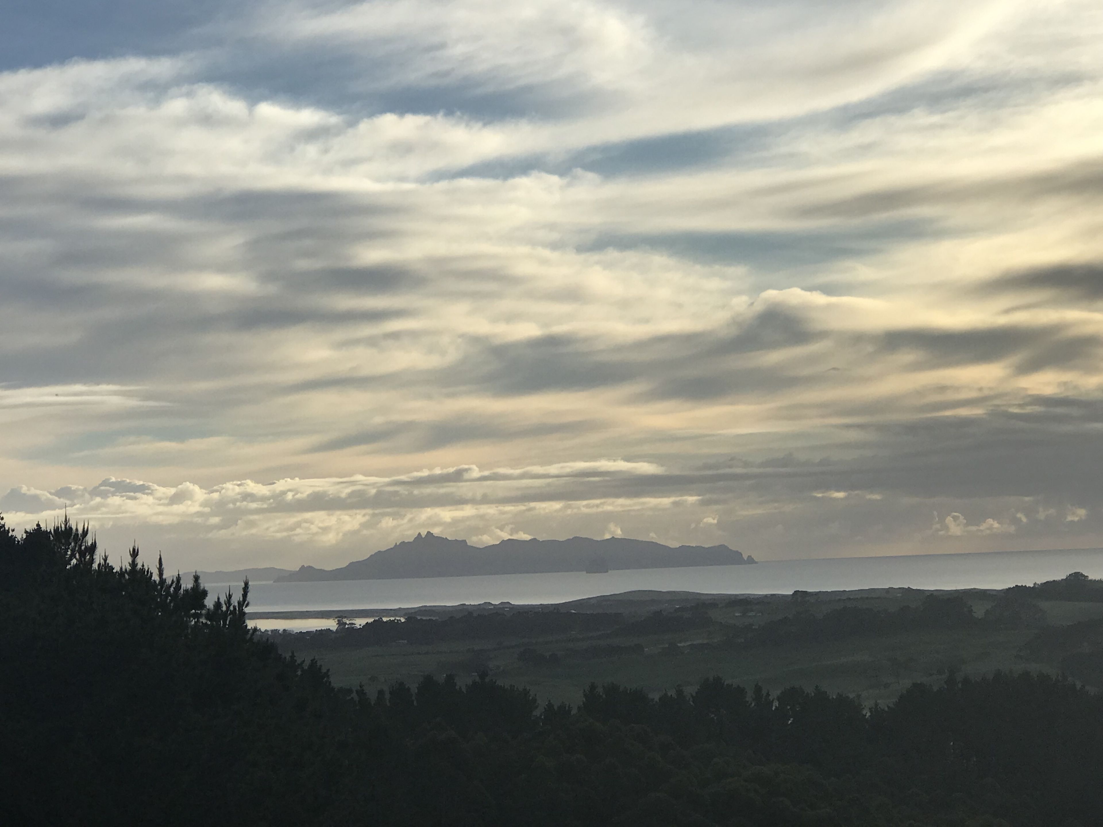 A landscape with a body of water, distant mountains, and a cloudy sky.