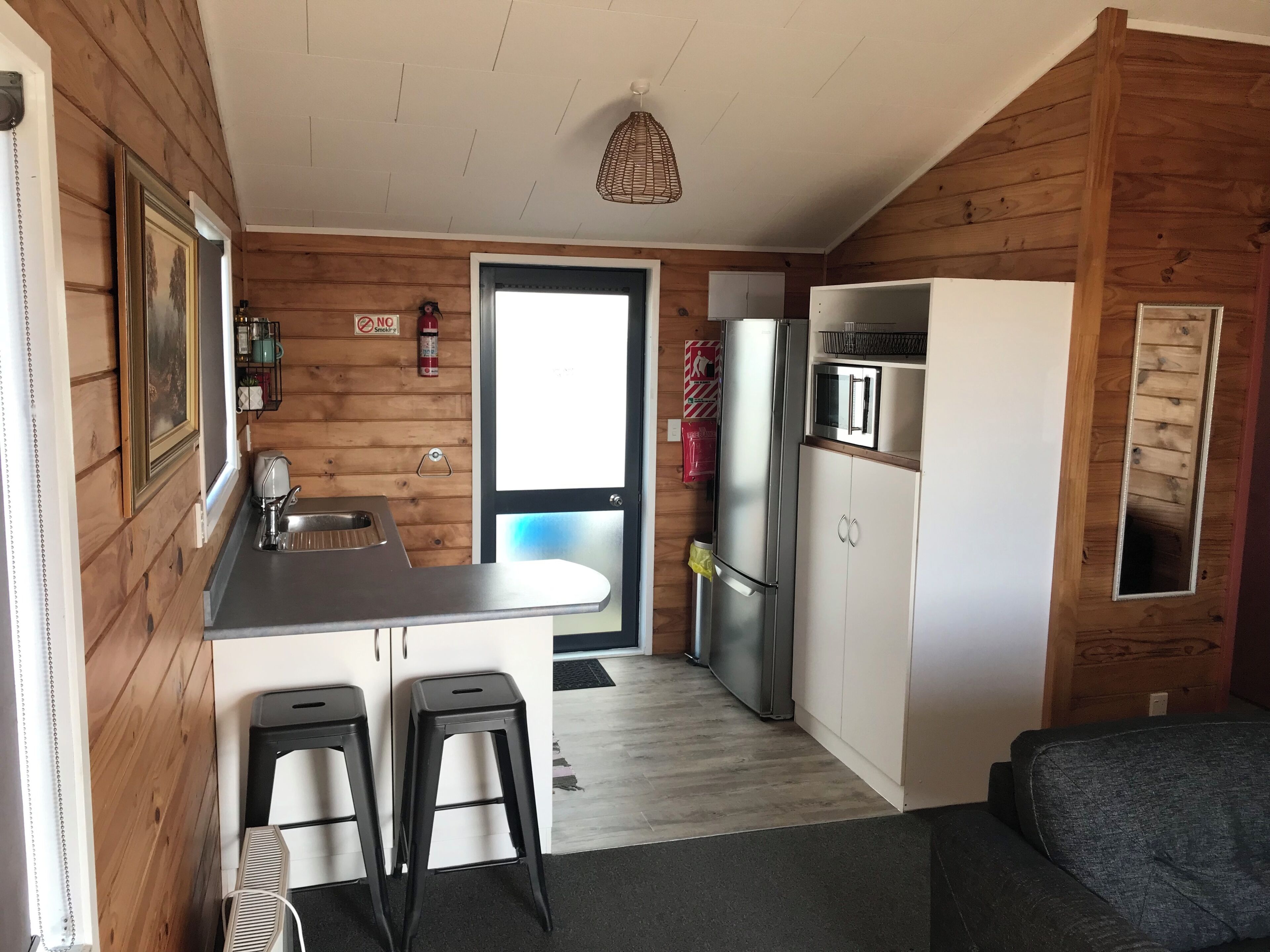 Una cocina compacta con paredes de madera, un refrigerador de acero inoxidable, un microondas y un lavamanos.
