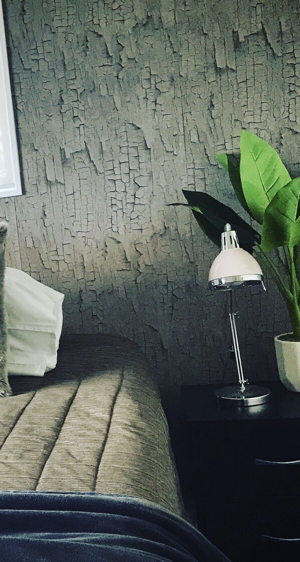 Une pièce avec un mur à texture, une lampe blanche posée sur une table d’appoint noire et une plante en pot.