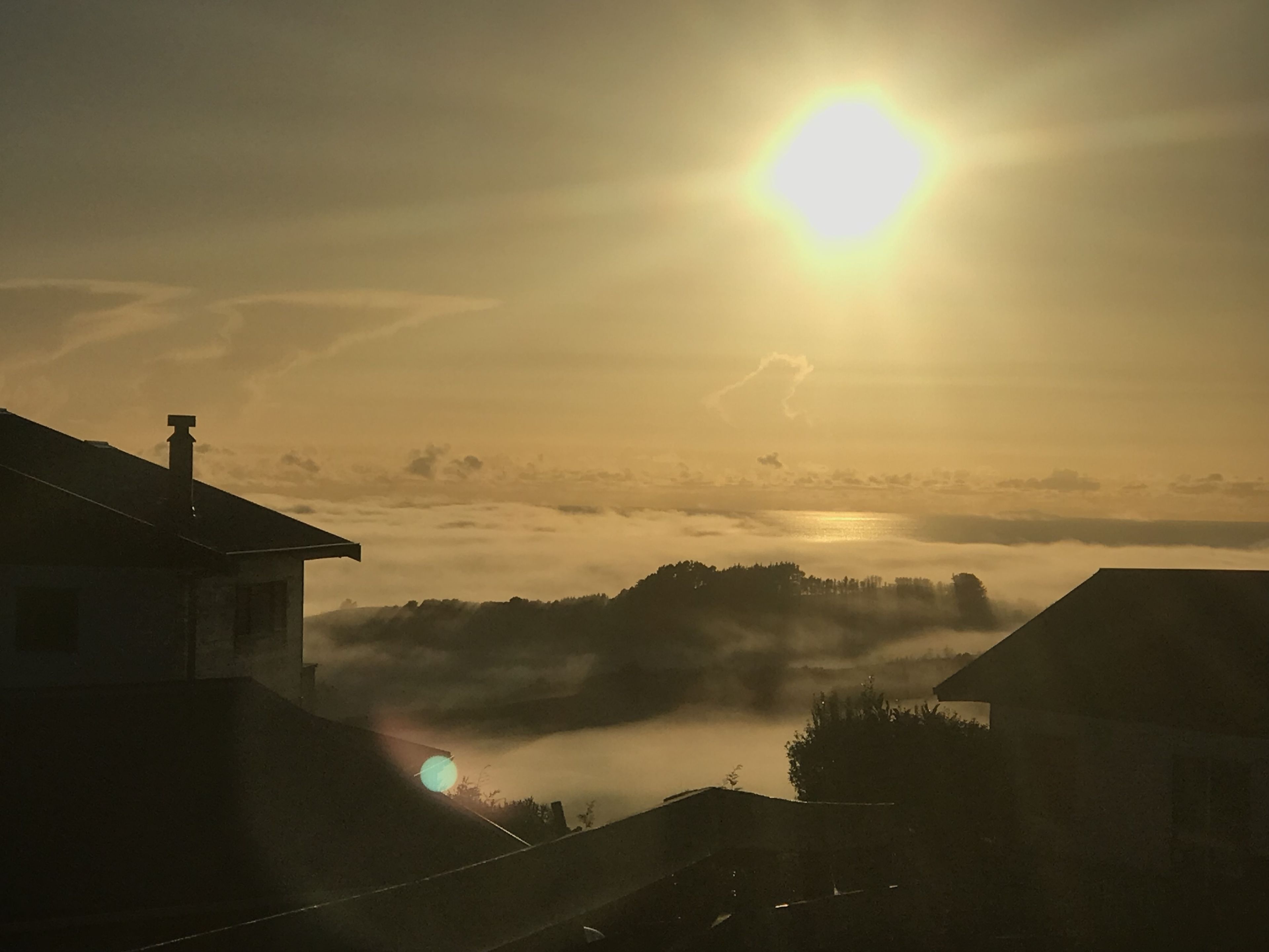 Un lever de soleil sur un paysage brumeux, avec des maisons se détachant en silhouette sur le ciel.