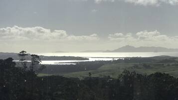 Paisagem costeira com um corpo de água, montanhas ao longe e uma área arborizada em primeiro plano.
