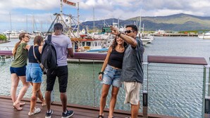 Un grupo de personas en un muelle con barcos y montañas al fondo.