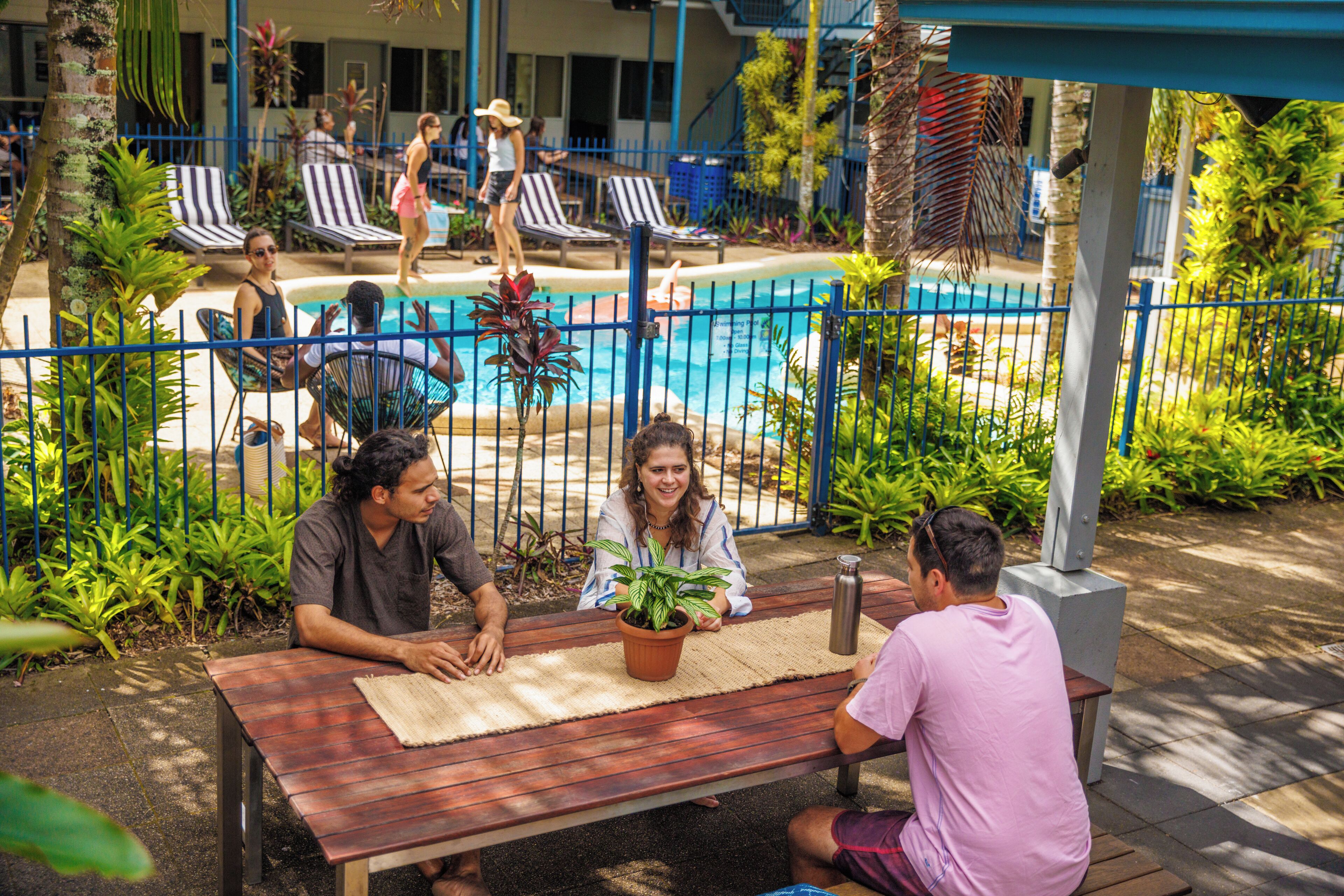 Un espace aménagé au bord de la piscine, avec des chaises longues, une table à manger et un pot de fleurs.