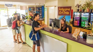 Zona de recepción con mostrador, computadora y letrero de Indigenous Eco Tours. Hay plantas en macetas y un refrigerador con bebidas.