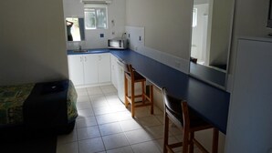 A compact kitchen with white cabinets, a blue countertop, a microwave, and a sink. There is a small window and a mirror above the countertop. - Chinderah Motel (Chinderah)