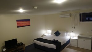 A hotel room with a bed, bedside lamps, a desk, a TV, and a painting on the wall. - Chinderah Motel (Chinderah)
