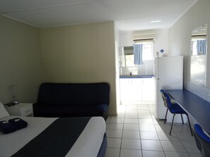 A hotel room with a bed, a desk, a chair, a small kitchenette, and a bathroom.