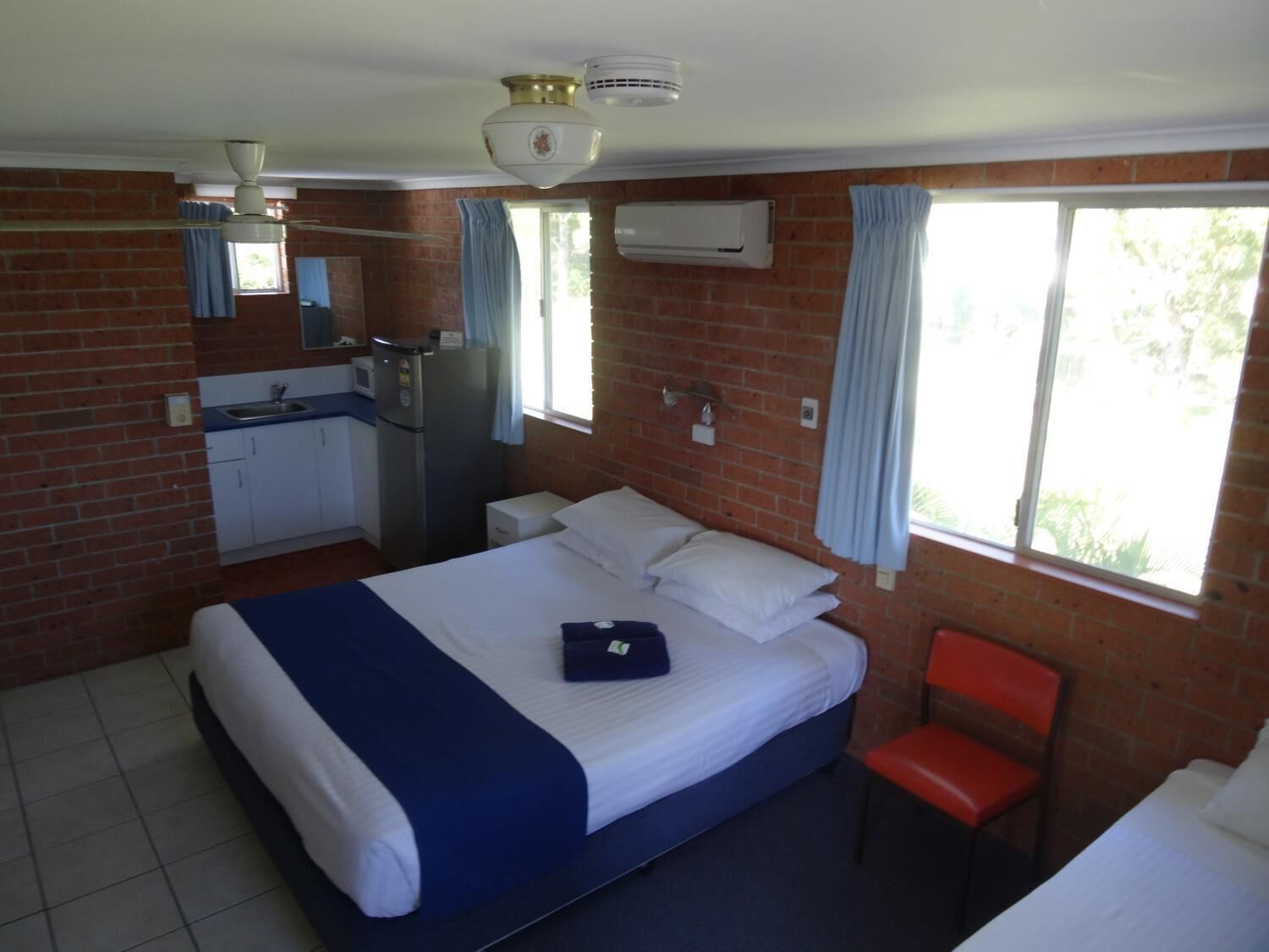 Una habitación con cama, una silla, una kitchenette pequeña y una ventana con cortinas.