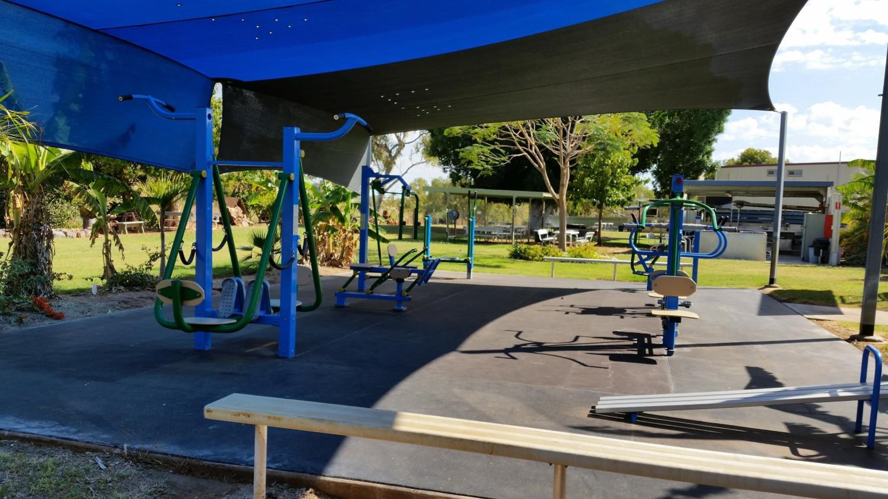 Un gimnasio al aire libre con diferentes equipos de ejercicio, incluyendo barras de dominadas y una banca.