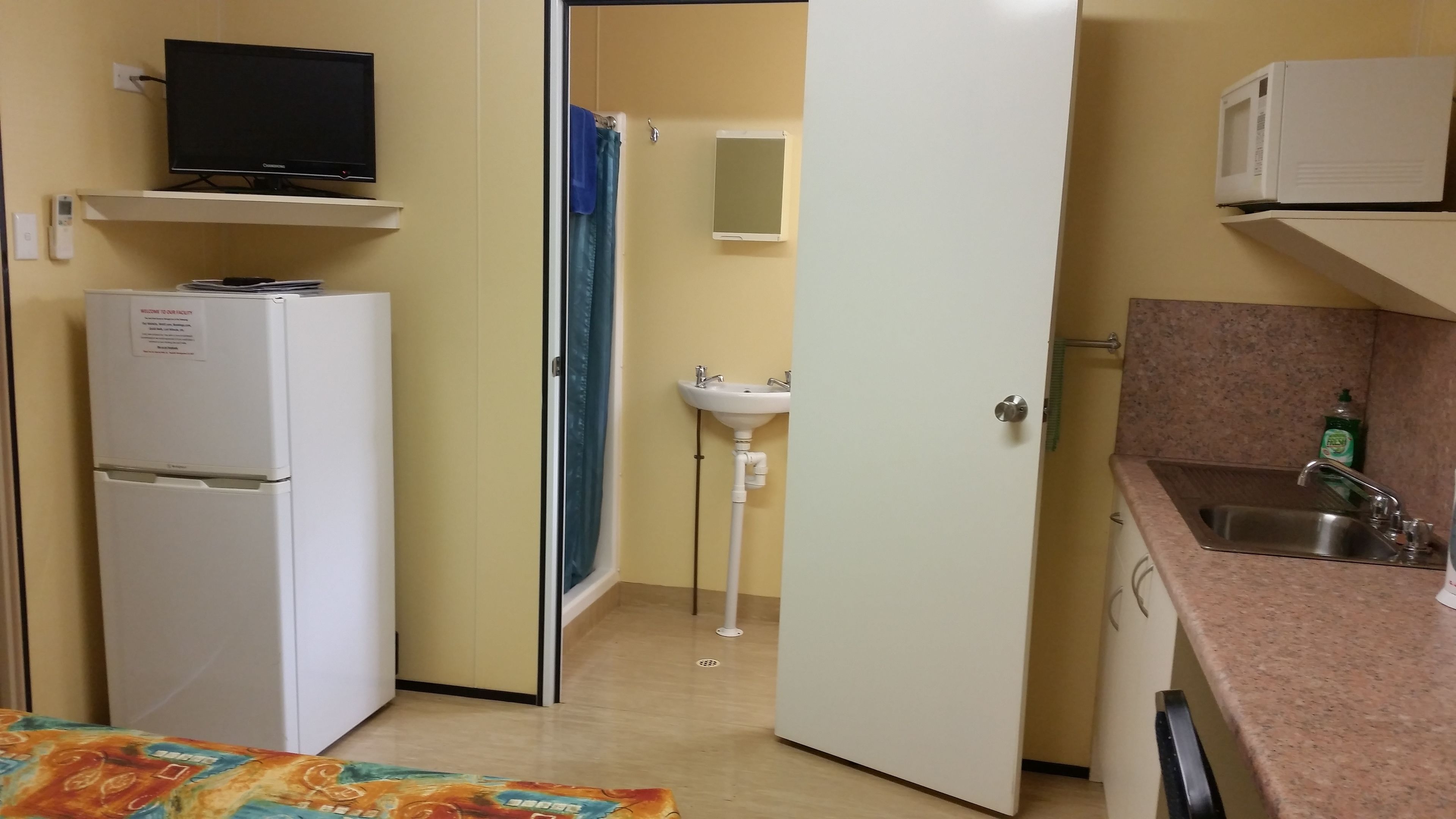 Habitación compacta con kitchenette, refrigerador, microondas, pileta y televisor en una estantería.