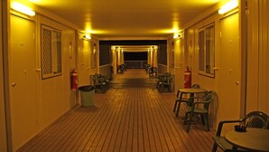 A corridor with doors numbered 29 and 26, leading to rooms. There are chairs and tables along the corridor, and a fire extinguisher is visible. - Leichhardt Accommodation (Mornington)