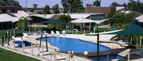 A swimming pool with lounge chairs and umbrellas, surrounded by a fence and greenery.