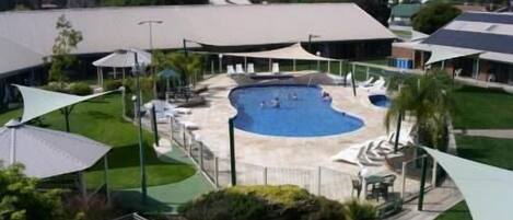 A swimming pool with a curved edge, surrounded by a covered patio area with seating and umbrellas.
