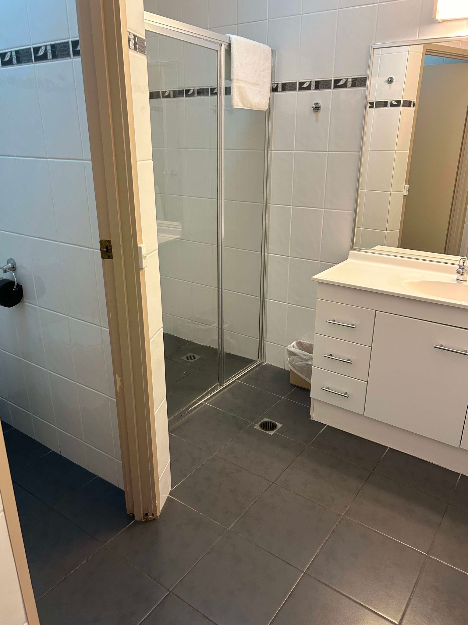 Un baño con cabina de ducha de vidrio, un lavabo blanco con espejo y piso de baldosas.