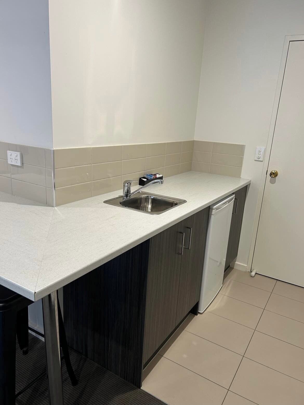 Una cocina moderna con un lavamanos de acero inoxidable, armarios de madera oscura y encimera blanca.